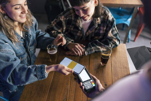 Smiling young woman paying through smart phone at restaurant - JSRF02212