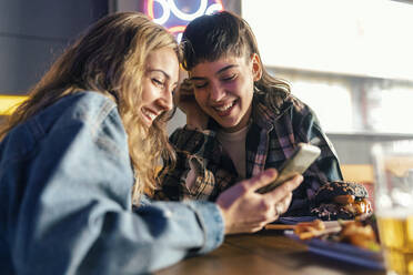 Cheerful lesbian couple using smart phone at table in restaurant - JSRF02215