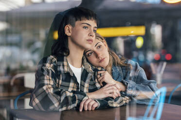 Thoughtful young lesbian couple sitting at table in restaurant - JSRF02224