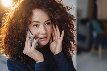 Schöne junge Frau mit lockigem Haar, die mit einem Smartphone telefoniert - JOSEF12841