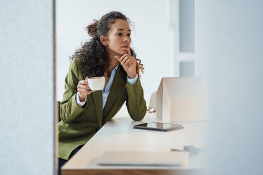 Thoughtful architect with coffee cup sitting at desk in office - JOSEF12869