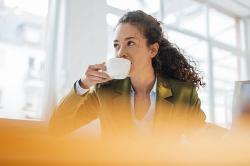 Junge Geschäftsfrau mit lockigem Haar trinkt Kaffee - JOSEF12876