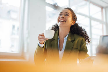 Fröhliche junge Geschäftsfrau mit Kaffeetasse im Büro - JOSEF12877