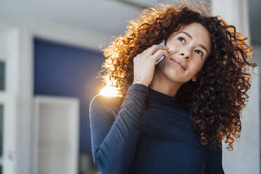 Nachdenkliche junge Frau mit lockigem Haar, die mit einem Smartphone telefoniert - JOSEF12878