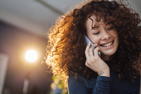 Glückliche schöne Frau mit lockigem Haar, die mit einem Handy telefoniert - JOSEF12879