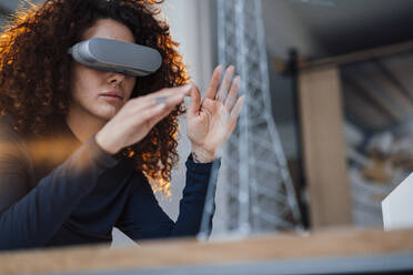 Young businesswoman wearing virtual reality simulator gesturing in office - JOSEF12885