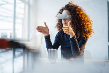Businesswoman wearing virtual reality simulator sitting with semiconductor at desk in office - JOSEF12888