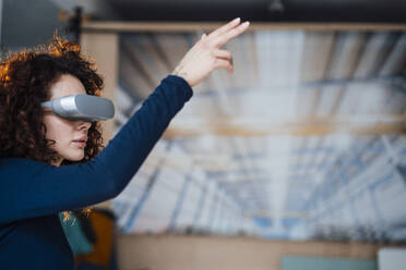 Businesswoman wearing wearing virtual reality simulator gesturing in office - JOSEF12890