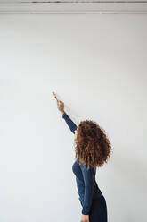 Junge Frau mit lockigem Haar benutzt Pinsel auf weißer Wand - JOSEF12905