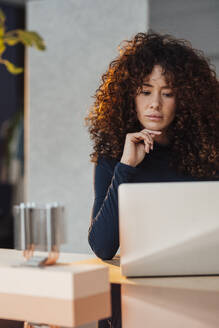 Businesswoman with hand on chin using laptop at desk in office - JOSEF12920