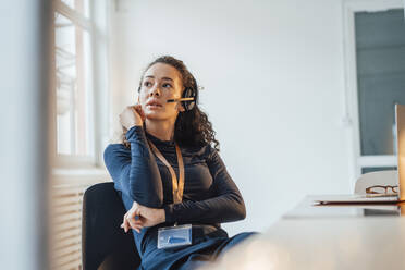 Junger Kundenbetreuer mit Headset sitzt am Schreibtisch im Büro - JOSEF12930