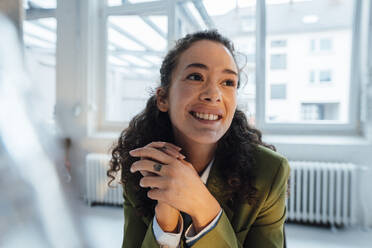 Happy young businesswoman with curly hair in office - JOSEF12949