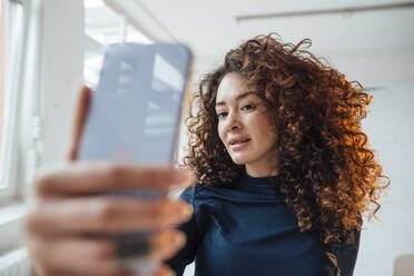 Junge Frau mit lockigem Haar nimmt durch Smartphone - JOSEF12968