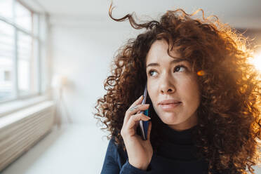 Beautiful woman with curly hair talking on smart phone contemplating - JOSEF12974