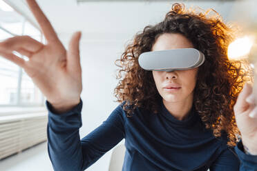 Businesswoman wearing virtual reality simulator gesturing in office - JOSEF12984