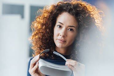Geschäftsfrau mit lockigem Haar, die einen Virtual-Reality-Simulator hält - JOSEF12987