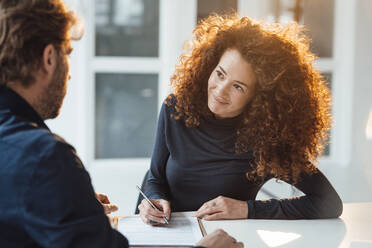 Smiling young businesswoman signing contract and looking at businessman in office - JOSEF13009