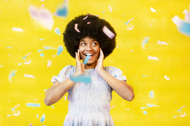 Happy young celebrating with confetti against yellow background - MMPF00259