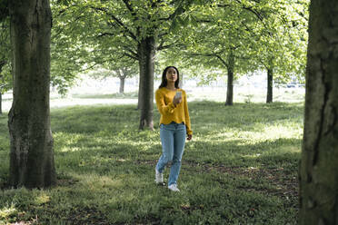 Junge Frau mit Smartphone beim Spaziergang im Park - AMWF00684