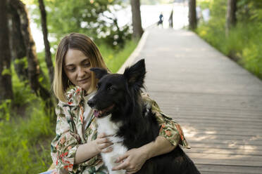 Junge Frau sitzt mit Hund an der Promenade im Park - SSGF00992