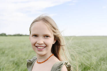 Happy girl with blond hair standing in grassy field - EYAF02132