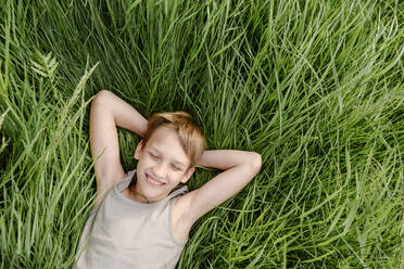 Happy boy with eyes closed lying down on grass - EYAF02134
