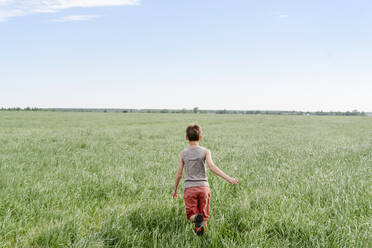 Junge rennt auf grasbewachsenem Feld am Himmel - EYAF02137