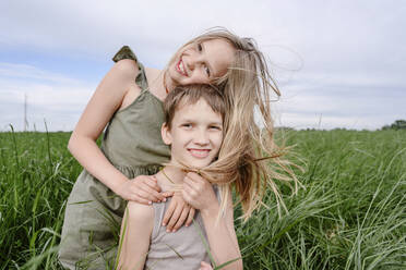 Happy brother and sister together at grassy field - EYAF02142