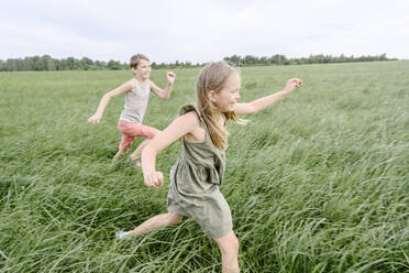 Happy siblings running on grass field - EYAF02147