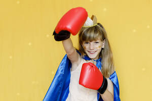 Glückliches Mädchen mit Boxhandschuhen und Umhang vor gelbem Hintergrund - TYF00379