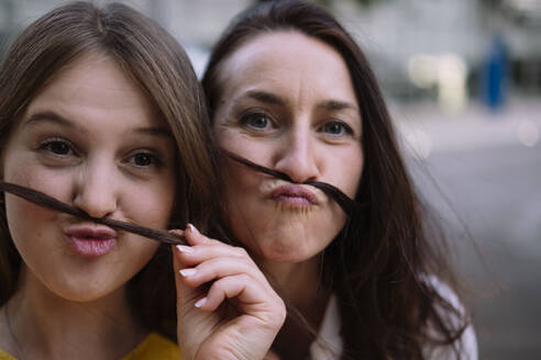 Zwei Frauen, die sich einen Spaß daraus machen, einen Schnurrbart mit Haaren zu machen - AMWF00740