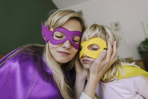 Mother and daughter with eyes closed wearing mask and cape at home - TYF00386