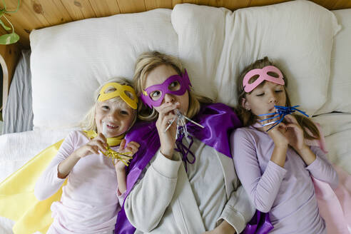 Mutter und Töchter mit Partyhornbläsern liegen zu Hause auf dem Bett - TYF00387