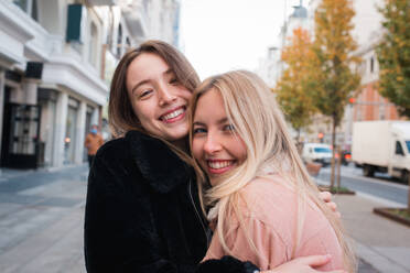 Charming young female best friends standing on street in Madrid and happily looking at camera - ADSF36312