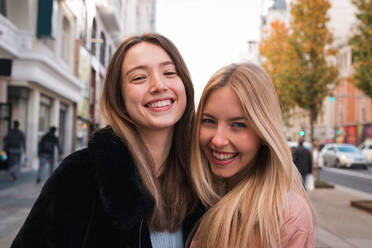 Charmante junge beste Freundinnen stehen auf der Straße in Madrid und schauen fröhlich in die Kamera - ADSF36313