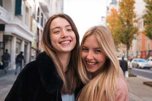 Charming young female best friends standing on street in Madrid and happily looking at camera - ADSF36313