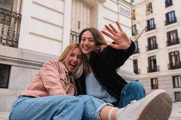 Fröhliche junge Freundinnen sitzen auf der Straße und haben Spaß zusammen, während sie das Wochenende in Madrid genießen - ADSF36317