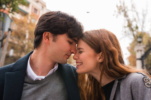 Affectionate young man and woman with eyes closed embracing each other gently while having romantic date on city street - ADSF36335