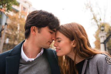 Affectionate young man and woman with eyes closed embracing each other gently while having romantic date on city street - ADSF36336