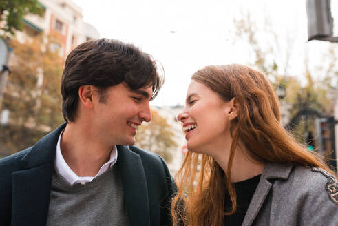 Fröhliche junge Frau, die sich mit ihrem Freund während eines romantischen Rendezvous auf einer Straße in der Stadt amüsiert und sich gegenseitig ansieht - ADSF36337