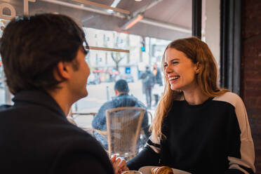 Seitenansicht der positiven liebevollen jungen Paar in der Liebe Blick auf einander, während am Tisch sitzen in der Nähe von Fenster in gemütlichen Café und genießen die Zeit zusammen - ADSF36349