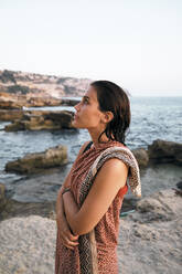 Thoughtful woman with arms crossed wrapped in blanket by sea - MMPF00271