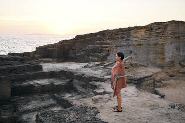 Contemplative woman wrapped in blanket standing by rock formations - MMPF00272