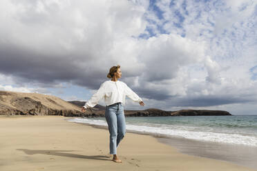 Young woman walking with arms outstretched at beach on sunny day - MRAF00897