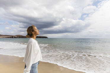 Woman with eyes closed standing by sea at beach - MRAF00908