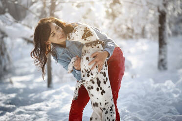 Lächelnde Frau umarmt Dalmatinerhund im Winterpark - AZF00440