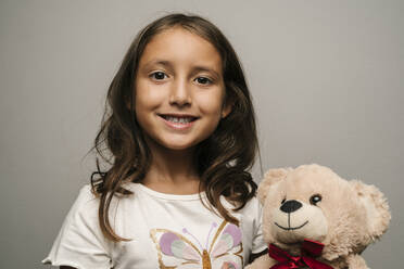 Smiling girl with teddy bear against gray background - EGAF02568