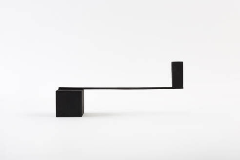 Black block balancing on thin plank on top of cube against while background - ADSF36374