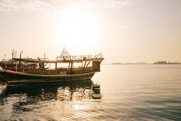 Authentisches Boot im Hafen auf kräuselndem Meerwasser gegen den Sonnenaufgangshimmel am Morgen in Doha, Katar - ADSF36378