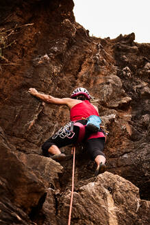 Low angle full length of active senior woman climbing on rocky cliff - ADSF36404